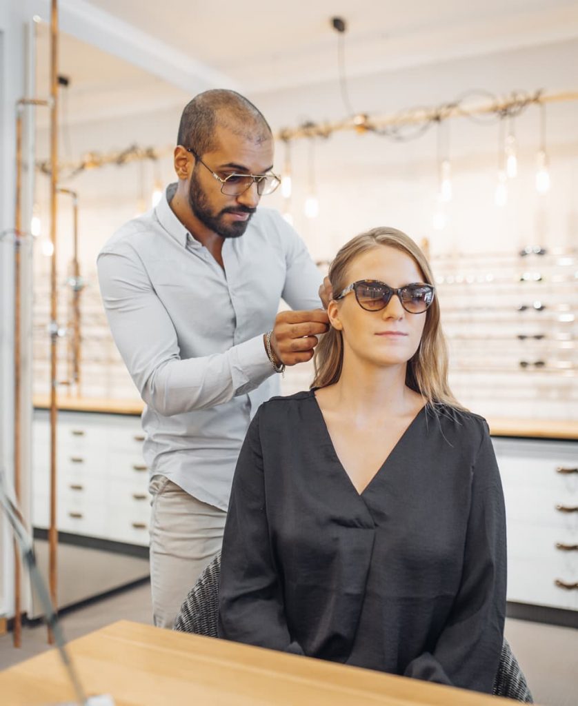 Optiker passt neue Sonnenbrille bei einer Kundin an